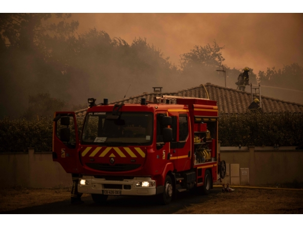 Firefighters spray water with a hose from the roof of a house during a wildfire near Lege Cap Ferret, southwestern France on July 23, 2026. (Photo by Julien De Rosa / AFP)
 