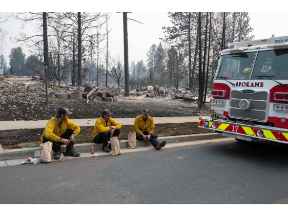 Three members of the Spokane Fire Department sit on a curb in front of burned out residential homes in the Balboa neighborhood of Spokane, Washington, on August 2, 2026. (Photo by Erick Doxey / AFP)