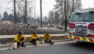 Three members of the Spokane Fire Department sit on a curb in front of burned out residential homes in the Balboa neighborhood of Spokane, Washington, on August 2, 2026. (Photo by Erick Doxey / AFP)