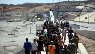 A group of migrants approach the border post to make their way back to Morocco, escorted by Spanish infantry soldiers, in the Spain's north African enclave of Ceuta, on August 2, 2026. Photo by Henry NICHOLLS / AFP