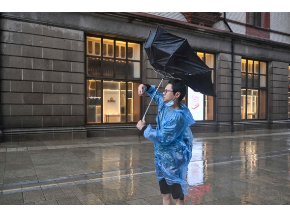 A man uses an umbrella to shelter from the rain on the Bund a day after Typhoon Dolphin made landfall in Shanghai on August 10, 2026. (Photo by Hector RETAMAL / AFP)