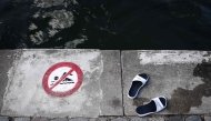 (FILES) This photograph shows sandals next to a sign indicating that swimming is forbidden, at the Bassin de la Villette during a cold water swimming event in Paris on March 29, 2025.(Photo by Thibaud MORITZ / AFP)