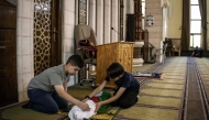 This photo taken on June 6, 2026 shows Kinan Abou Haikal (L), the elder brother of seven-month-old baby Sam Fahd Abou Haikal, sitting next to his body at the Abou Heisheh Mosque in Hebron, in the Israeli-occupied West Bank. (Photo by JOHN WESSELS / AFP)