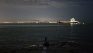 An angler (C) uses a headlamp before casting his line, as a large cargo container ship sails towards the Laem Chabang Port, near the city of Pattaya on September 1, 2026. (Photo by ANTHONY WALLACE / AFP)