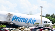 A parking lot filled with Tesla Cybercabs is seen in the foreground as the nose of a Prime Air cargo plane rests on the ground after the aircraft overran the runway and struck cars the previous day at Miami International Airport in Miami, Florida, on September 7, 2026. (Photo by CHANDAN KHANNA / AFP)