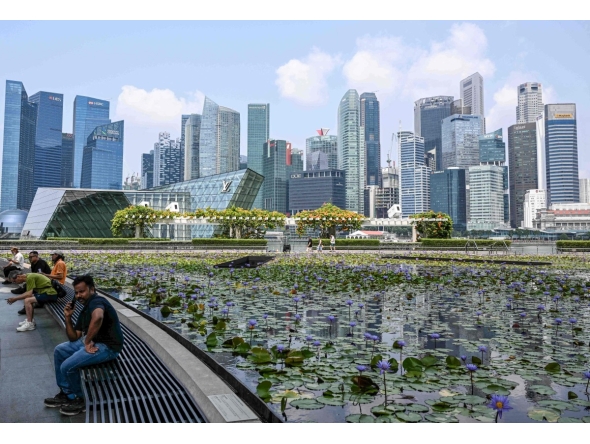 People sit next to a pond outside ArtScience museum at Marina bay in Singapore on September 8, 2026. (Photo by Roslan RAHMAN / AFP)