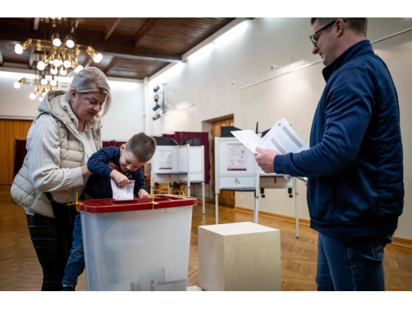 A child accompanied by his parents casts a ballot at a polling station during Latvia's parliamentary elections in Riga on October 3, 2026. (Photo by Wojtek Radwanski / AFP)