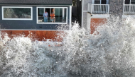 In an aerial view, people watch from a home as a Pacific Ocean wave crashes into a seawall protecting homes amid powerful surf on October 9, 2026 in Long Beach, California. (Photo by Mario Tama/Getty Images/AFP ) 