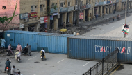Commuters gather at a road blocked with shipping containers amid ongoing protests by the opposition Pakistan Tehreek-e-Insaf (PTI) party demanding the release of jailed former prime minister Imran Khan in Peshawar on October 11, 2026. (Photo by Abdul Majeed / AFP)