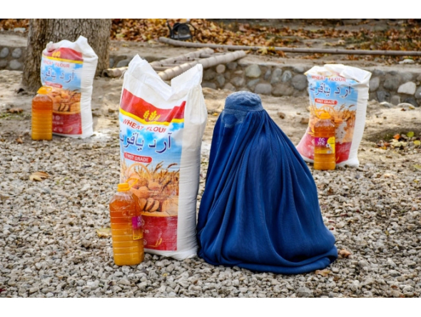 An Afghan burqa-clad woman sits next to food aid distributed by a local charity foundation in Mazar-i-Sharif. (AFP)