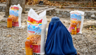 An Afghan burqa-clad woman sits next to food aid distributed by a local charity foundation in Mazar-i-Sharif. (AFP)