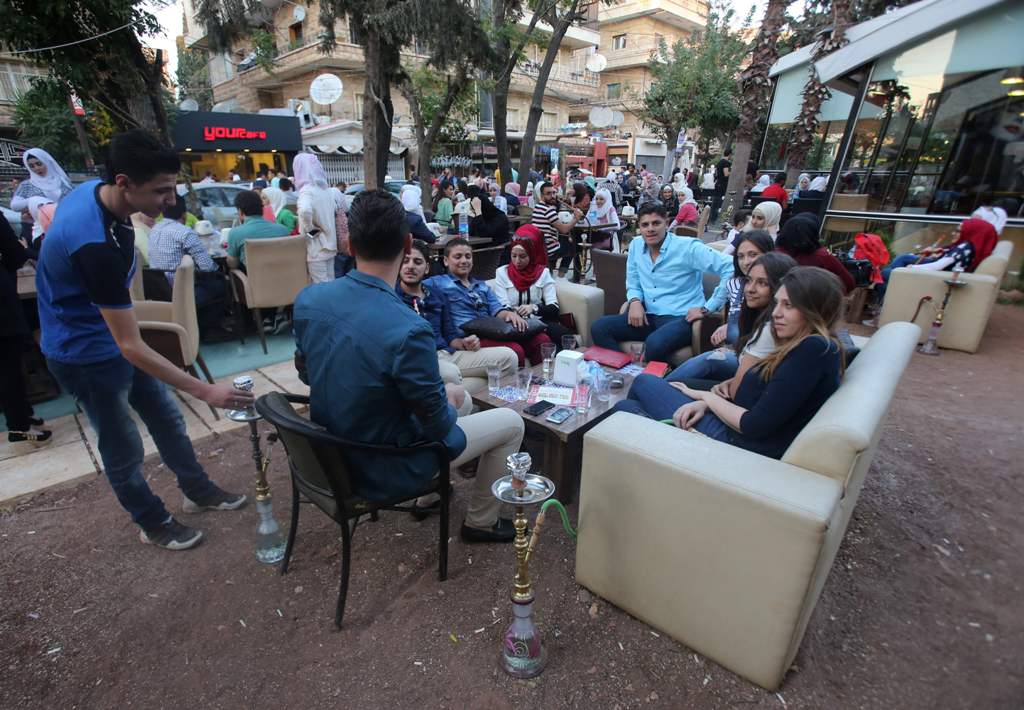 Syrian youths sits at a cafe in the government-held area of the northern Syrian city of Aleppo as they celebrate the Eid al-Adha Muslim holiday on September 13, 2016, a day after a fragile ceasefire was brokered.  AFP / Youssef KARWASHAN
