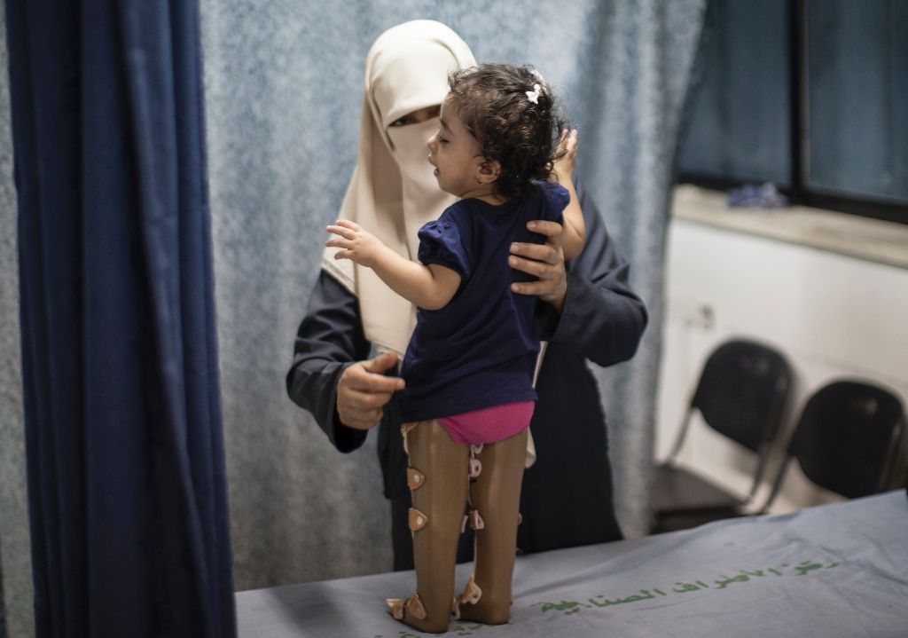 A woman supports her child as she tries to stand in prosthetic legs at Gaza's Artificial Limbs and Polio Centre (AFP Photo/Mahmud Hams)