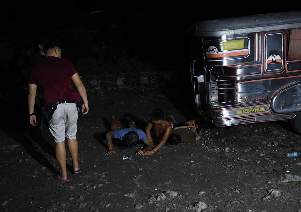 A police officer (L) in civilian clothes watches suspected drug users arrested during a drug buy-bust operation by police along a rail line in Caloocan City suburban Manila on early September 30, 2016. Philippine President Rodrigo Duterte on September 30 
