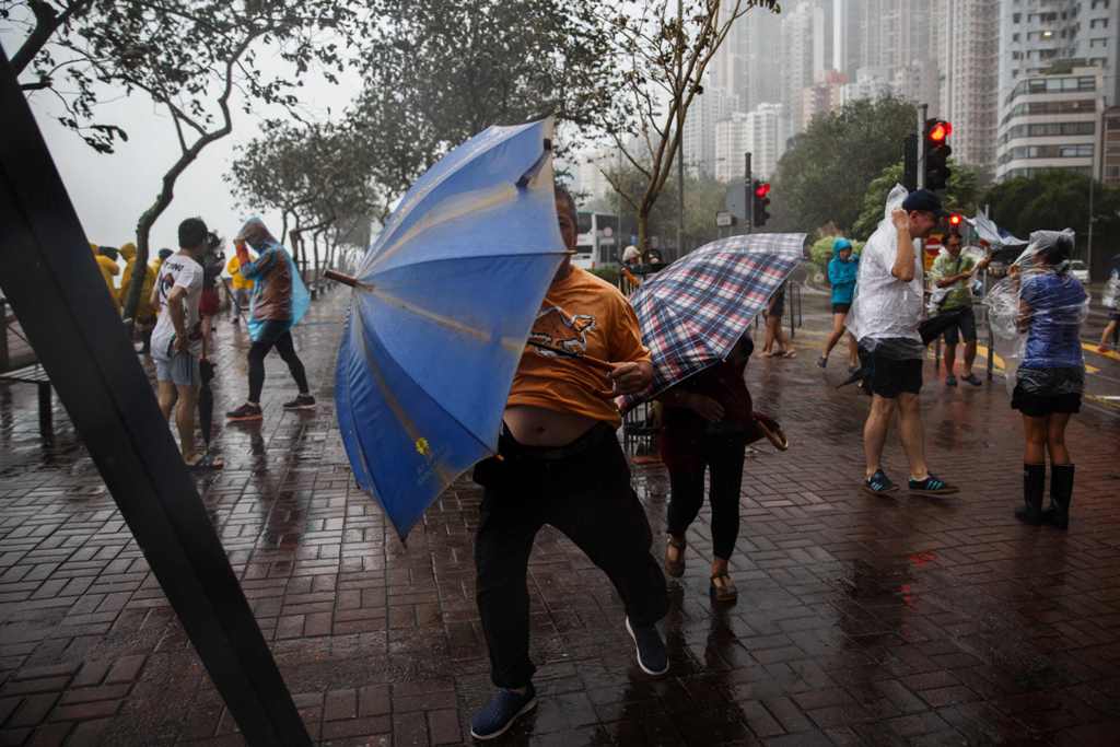 People use their umbrellas near a coastal barrier as Typhoon Haima makes landfall Hong Kong on October 21, 2016, during a typhoon signal eight warning.  AFP / ANTHONY WALLACE
