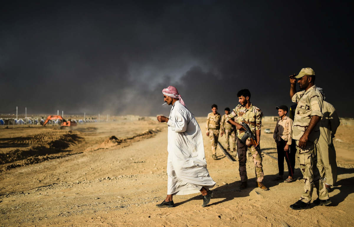 A displaced Iraqi man walks past security forces at a refugee camp on October 22, 2016 in the town of Qayyarah, south of Mosul, as an operation to recapture the city of Mosul from the Islamic State group takes place. Iraqi security forces battled for a se