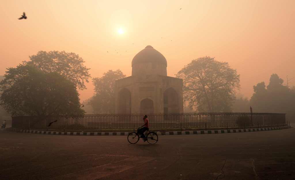 An Indian cyclist rides along a street as smog envelops a monument in New Delhi on October 31, 2016, the day after the Diwali festival. AFP / MONEY SHARMA