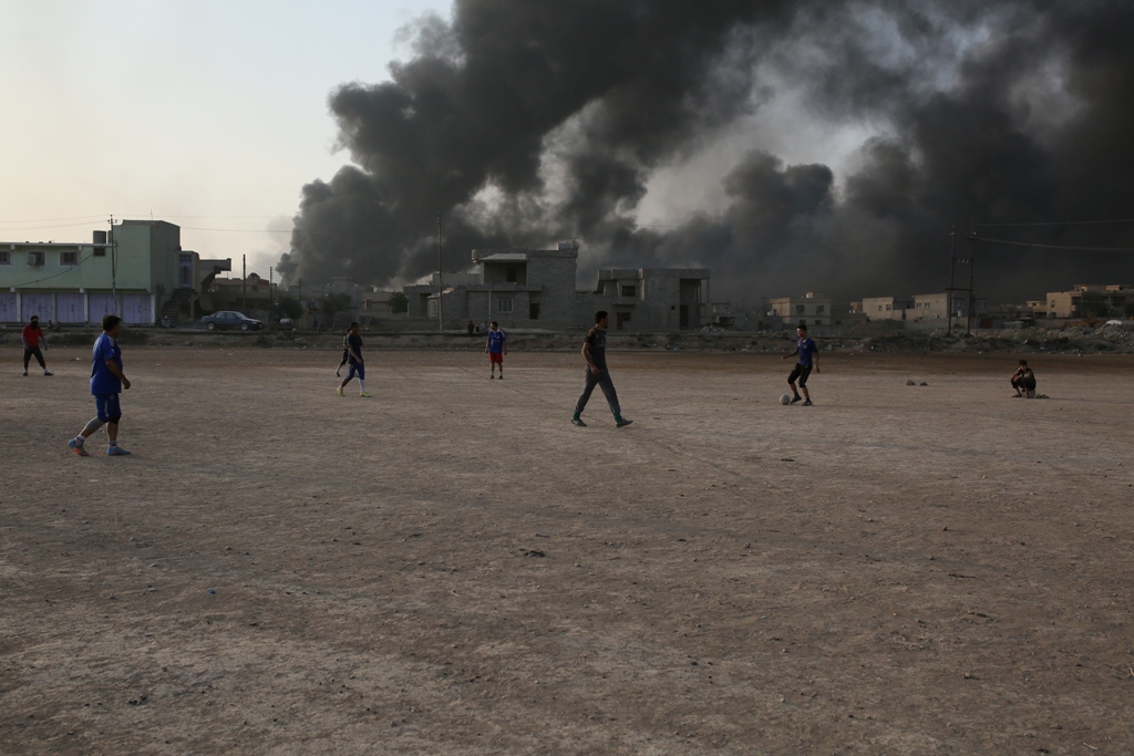Children play football as smoke rises from oil wells, were set on fire by Islamic State to limit coalition forces pilots' eyesight and to make the wells out of service following Iraqi army's retaking of Al Qayyarah town from Islamic State during the opera