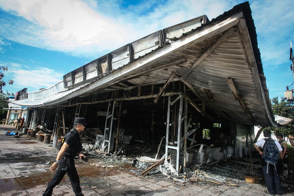 A police officer walks past a 7-11 convenience store in the Thai southern province of Pattani on November 3, 2016, after it was damaged in a bombing the night before. AFP / TUWAEDANIYA MERINGING