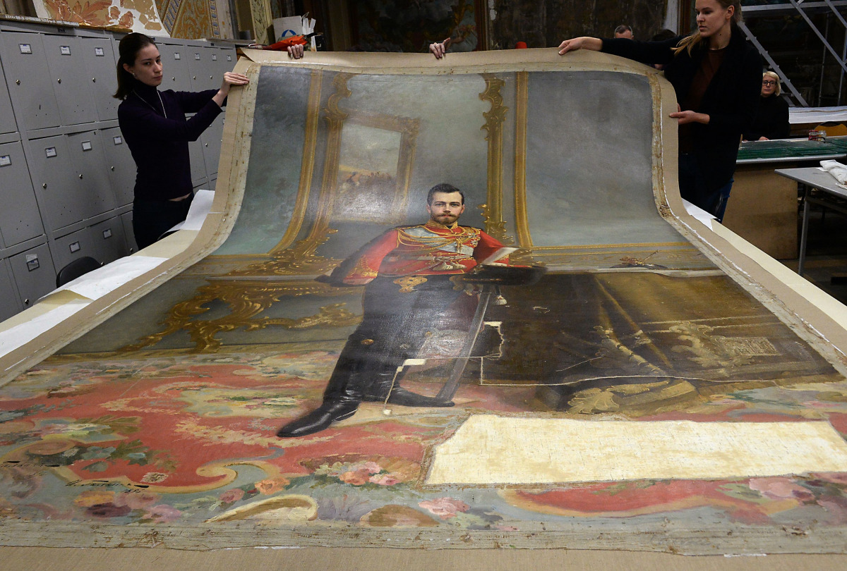 A picture taken in Saint Petersburg on November 17, 2016 shows restorers of the Stieglitz Art and Industry Academy displaying the portrait of Tsar Nicholas II by Ilya Galkin (1896) that was discovered beneath water-soluble paint on the back of the canvas 