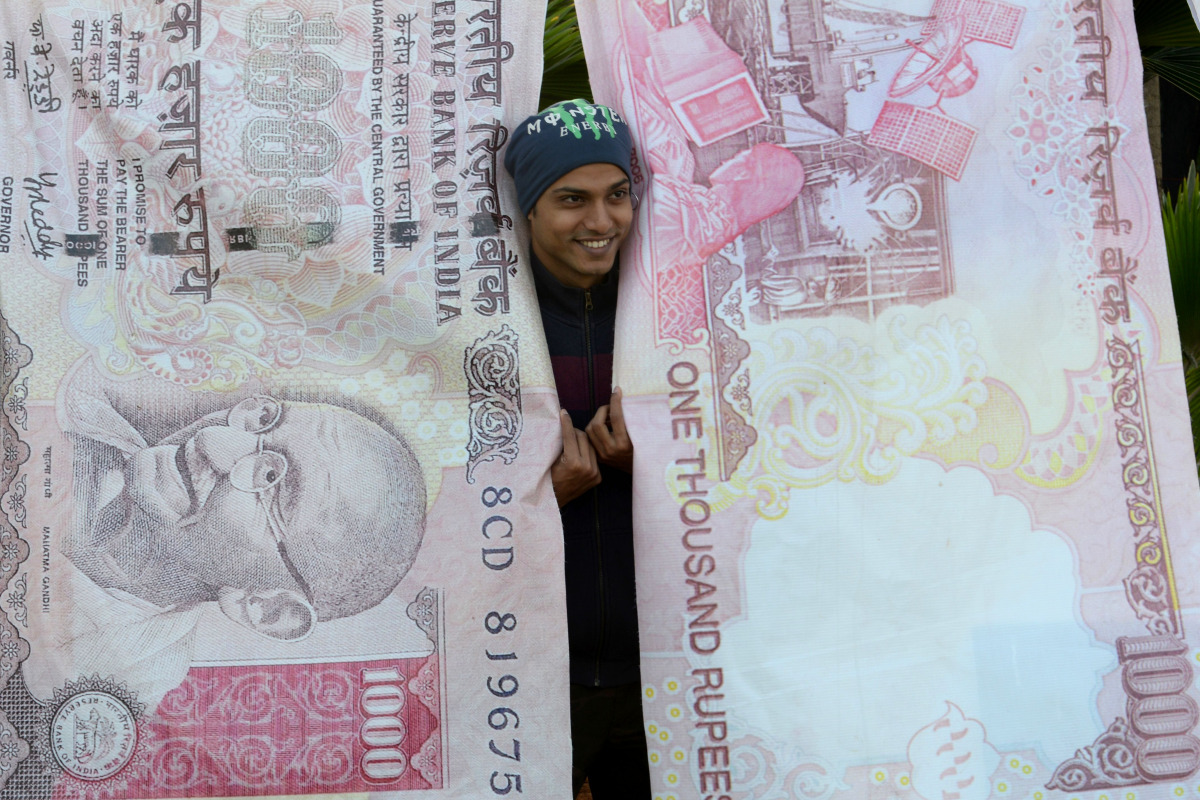 A man poses with replica prints of the demonetised 500 and 1000 rupee notes as part of a street art exhibition in Mumbai on November 20, 2016. (AFP / Indranil MUKHERJEE)
