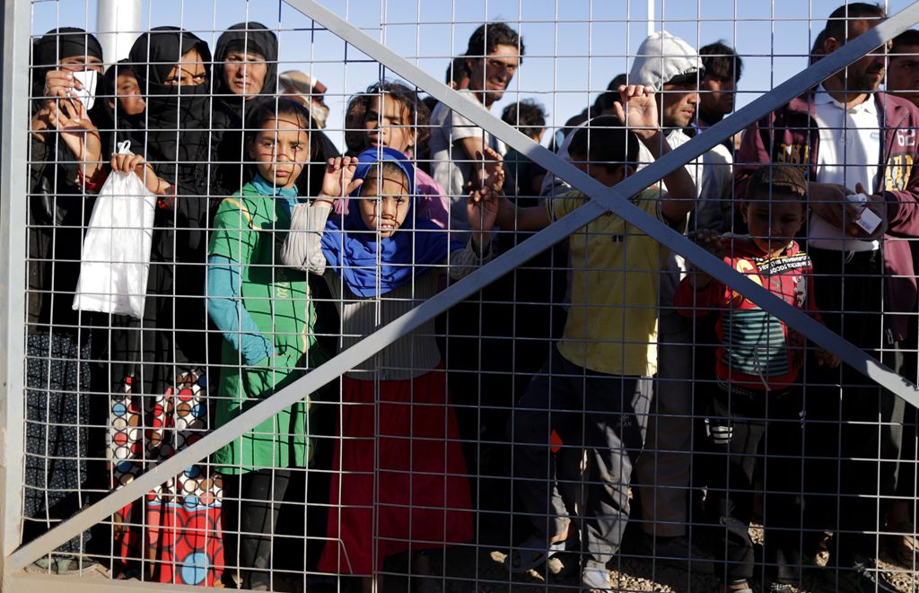 Iraqi refugees wait behind a fenced gate for food distribution at the Khazir refugee camp near the Kurdish checkpoint of Aski Kalak, 40 km West of Arbil, the capital of the autonomous Kurdish region of northern Iraq, on November 21, 2016. / AFP