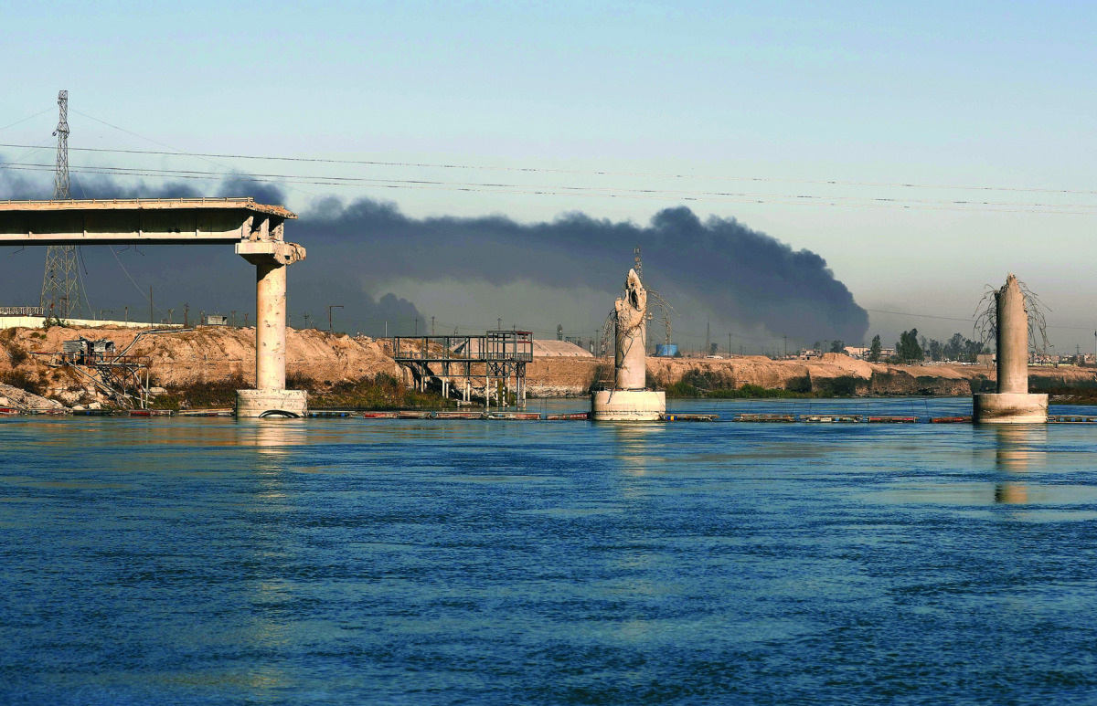 A bridge destroyed by Islamic State (IS) group is seen in front of black plumes of smoke from burning oil wells, set ablaze by retreating militants, in Qayyarah, some 60km south of Mosul, Iraq, yesterday.