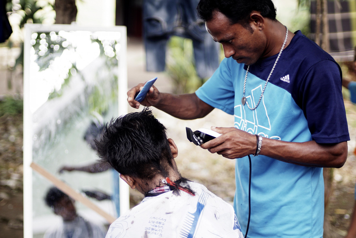 A Rohingya refugee man cuts the hair of a kid at a temporary shelter in Beras Pati after arrived from Aceh Shelter, in Medan of North Sumatra, Indonesia on November 25, 2016. About 164 Rohingyas are accommodated by the Indonesian Government arrived in Ber