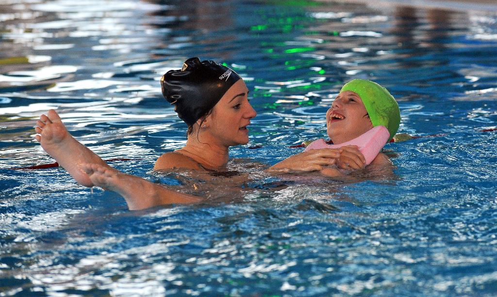 A Bosnian swim coach (L) swims with a disabled child during a training session on November 22, 2016, at Sarajevo's Olympic Swimming Pool facility. AFP / ELVIS BARUKCIC