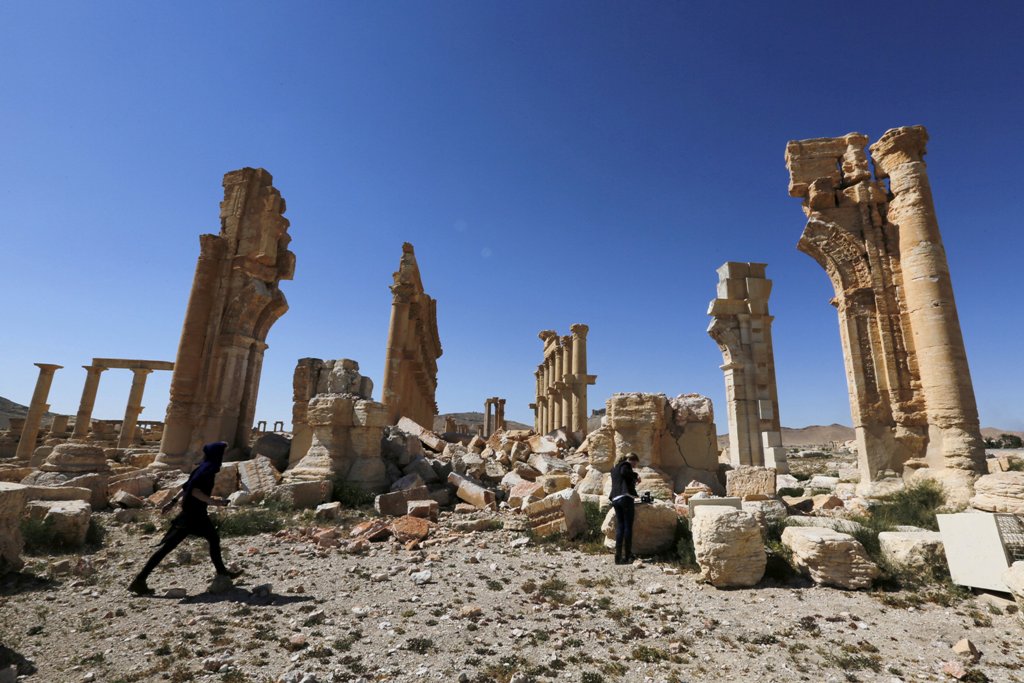 Journalists walk near the remains of the Monumental Arch in the historical city of Palmyra, in Homs Governorate, Syria April 1, 2016. REUTERS/Omar Sanadiki/File Photo