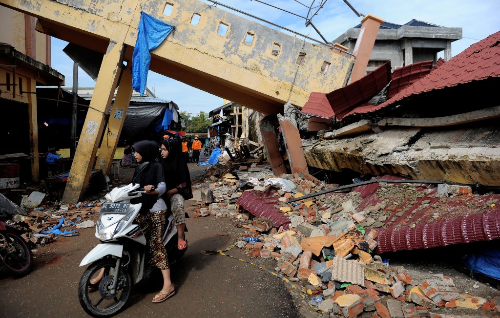 This picture taken on December 12, 2016 shows two girls on a motorcycle as they pass a collapsed building after a 6.5-magnitude earthquake struck the town of Pidie, Indonesia's Aceh province in northern Sumatra, on December 7, 2016.  AFP / CHAIDEER MAHYUD