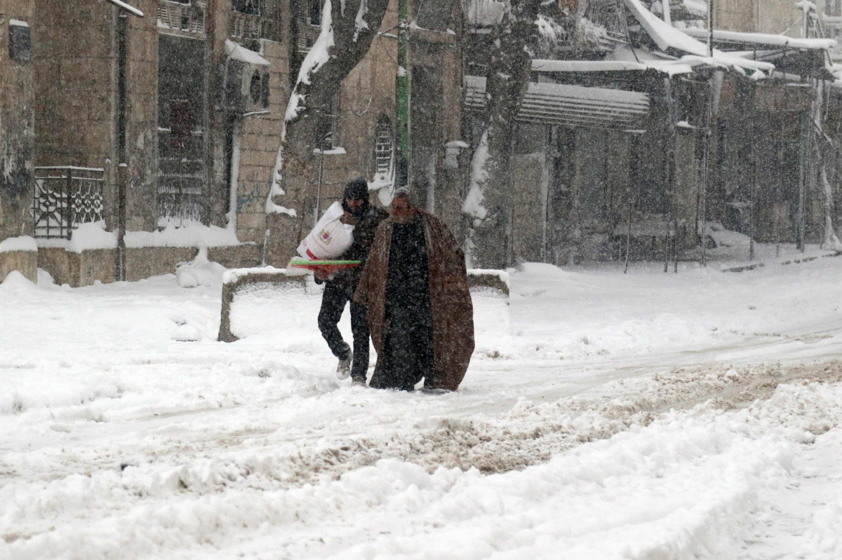  Syrians walk in a snow covered street in the town of Maaret al-Numan, in Syria's northern province of Idlib, on December 21, 2016. Rebels and civilians who have sought refuge in the opposition-held province of Idlib, most recently from second city Aleppo