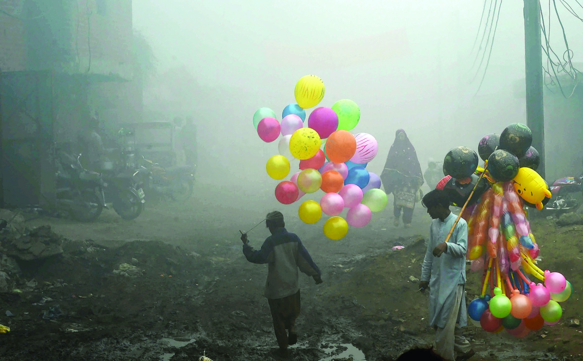 Pakistani balloon vendors cross a street in heavy fog in Lahore on December 24, 2016. / AFP / ARIF ALI