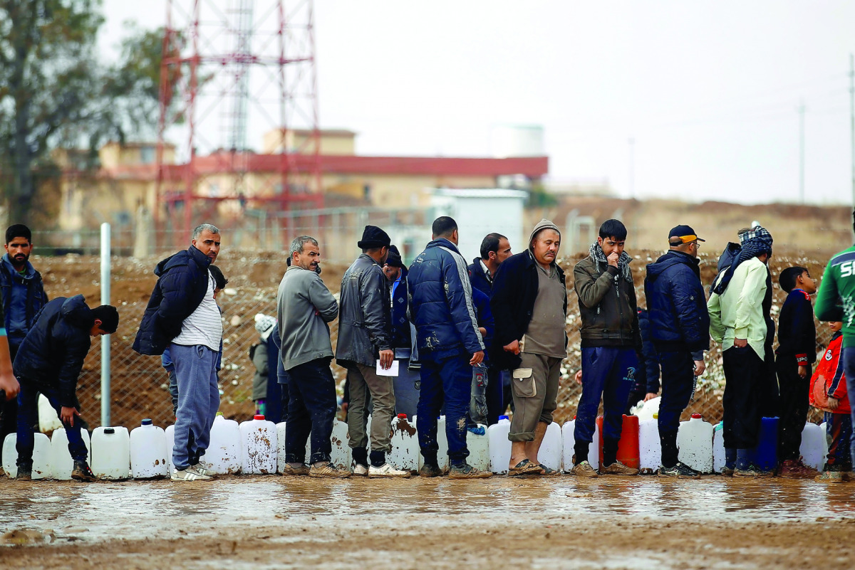 Displaced Iraqis, who fled the Islamic State stronghold of Mosul, carry empty containers as they wait in line to fill them with fuel to be used for cooking and lighting at Khazer camp in Iraq, yesterday. 
