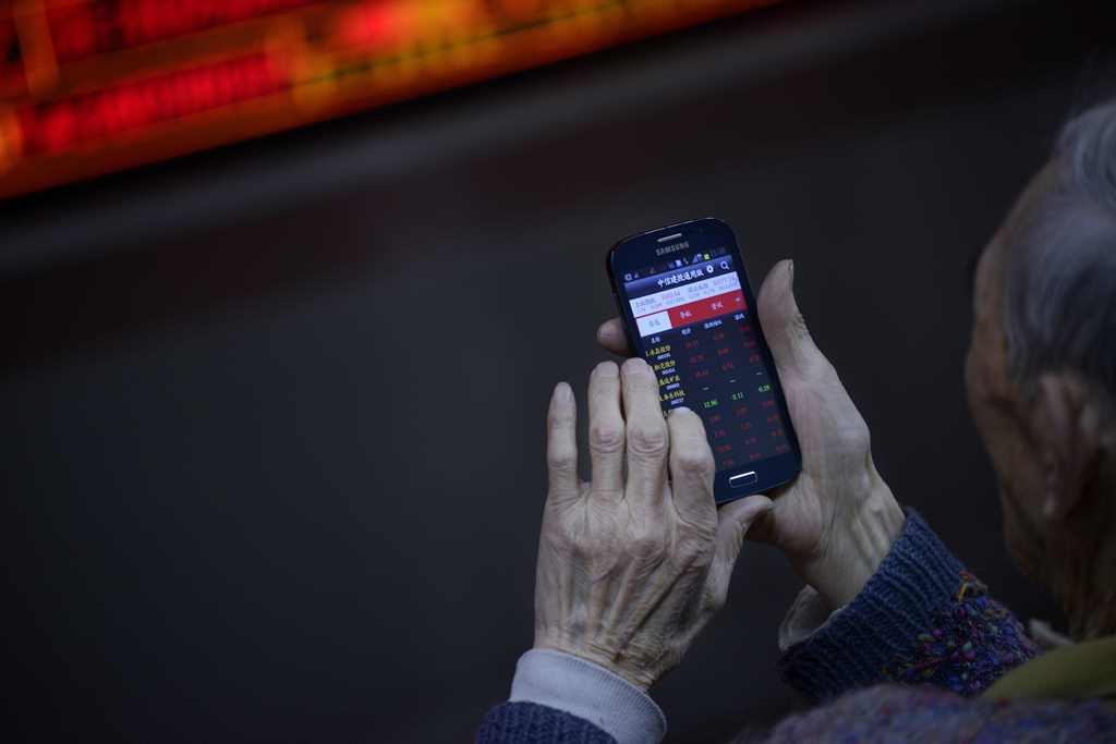 An investor uses a mobile phone to check stock indexes at a securities company in Beijing on January 3, 2017. AFP / WANG Zhao
