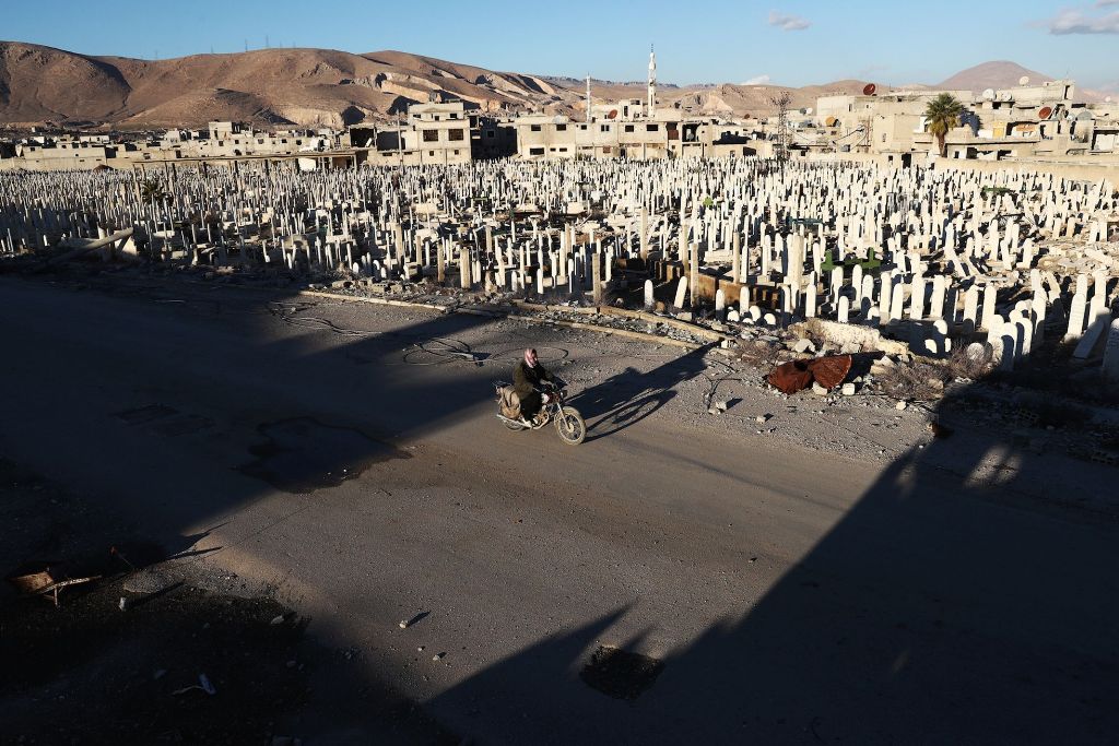 A Syrian man rides a motorbike past a cemetery in the rebel-held town of Douma, on the eastern outskirts of Damascus, on January 3, 2017. / AFP / Abd Doumany
