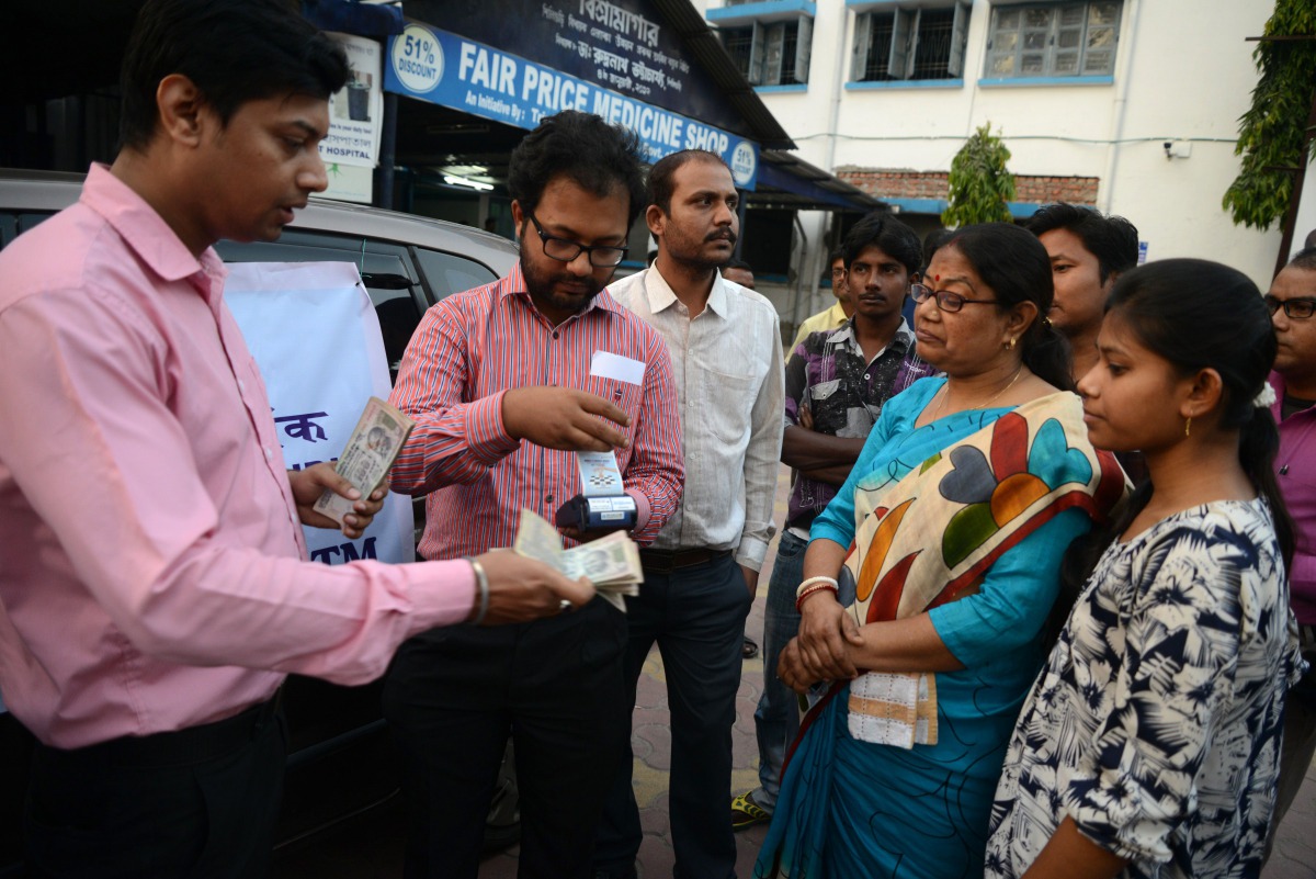 State Bank of India staff assist customers to withdraw money with the use of a mobile banking machine at Siliguri District hospital in Siliguri on November 22, 2016 (AFP / Diptendu DUTTA) 