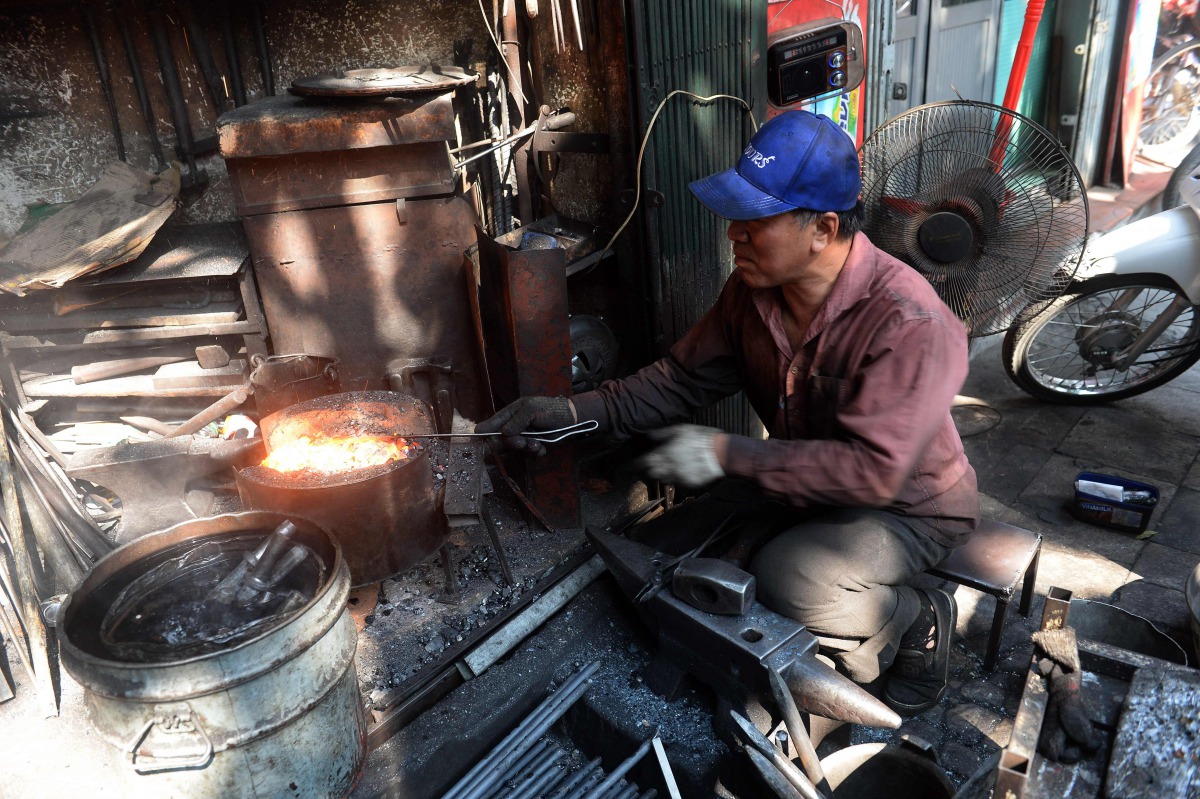 Nguyen Phuong Hung working at his shop on Lo Ren street in downtown Hanoi on December 8, 2016. Sitting before a bright orange flame, he prods a fire pit with a long metal rod before he hammers, bends, and contorts glowing steel into a giant drill bit. Hun