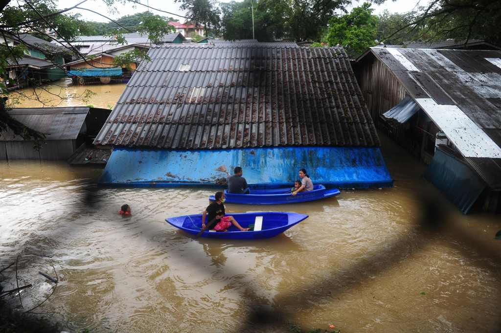 This photo taken on January 2, 2017 shows people navigating floodwaters by boat after heavy rains in Sungai Kolok district in the southern Thai province of Narathiwat. / AFP / MADAREE TOHLALA.