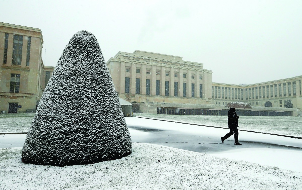 A staff member walks under a snowfall on a winter morning at the European headquarters of the United Nations in Geneva, Switzerland, yesterday.