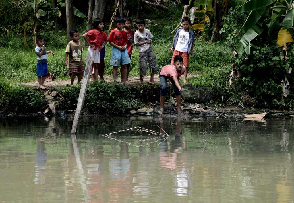 This picture taken on December 22, 2016 shows a group of Indonesian children trying to catch fish on the banks of one of the tributaries of the Ciliwung river in the Indonesian capital Jakarta. AFP / GOH CHAI HIN
