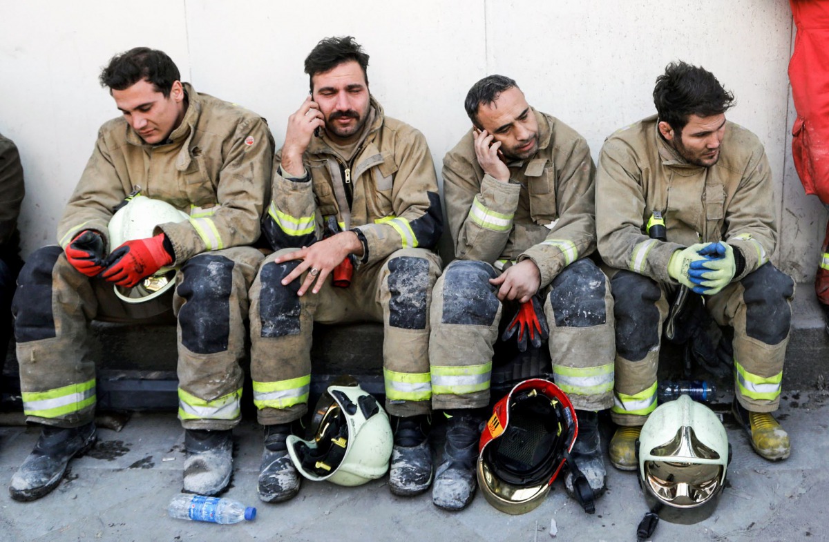 Iranian emergency personnel mourn for lost colleagues and friends as they sit in front of the wreckage of the 15-storey Plasco building which collapsed the previous day, on January 20, 2017, in the capital Tehran. Iranian officials said they were losing h