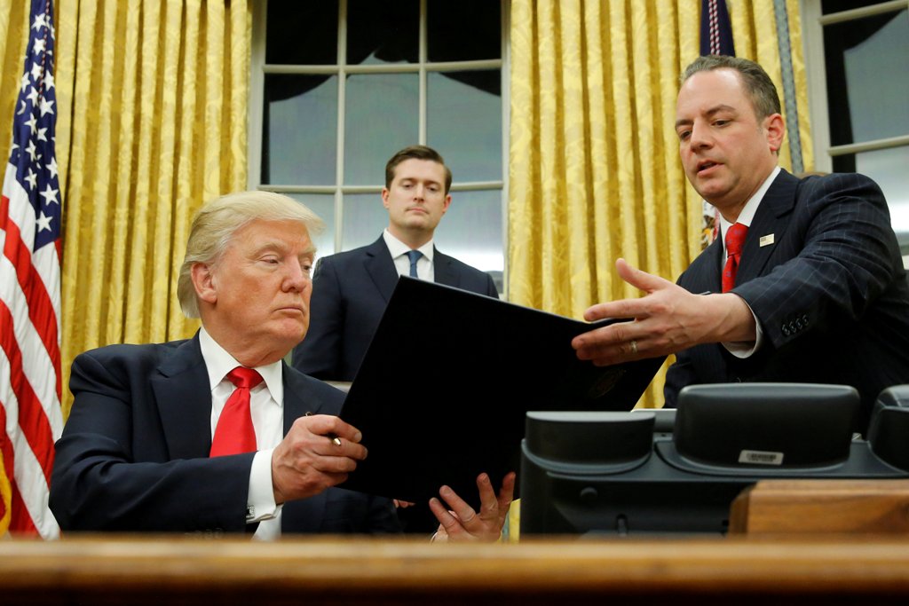 U.S. President Donald Trump hands Chief of Staff Reince Priebus (R) an executive order that directs agencies to ease the burden of Obamacare, after signing it in the Oval Office in Washington, U.S. January 20, 2017. REUTERS/Jonathan Ernst 
