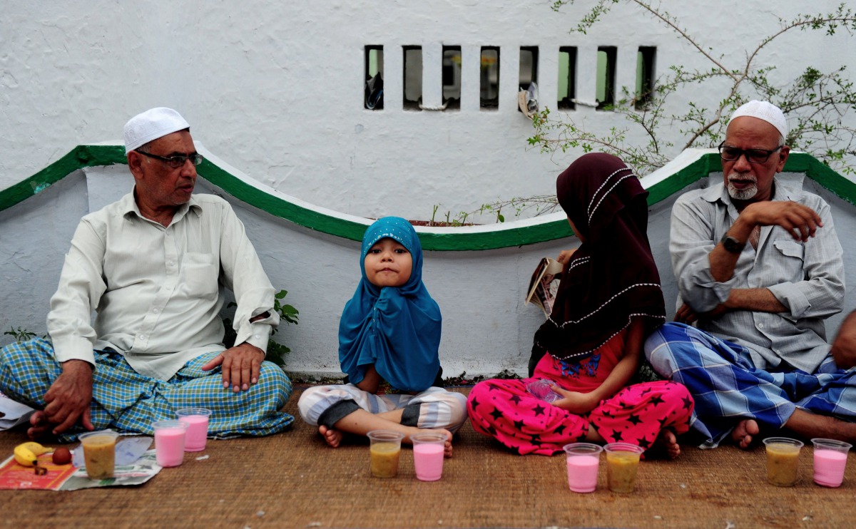 A young child sits with her guardians as they prepare to break the fast with the Iftar meal during Ramadan at The Wallajah Big Mosque in Chennai on July 1, 2016 (Reuters) 