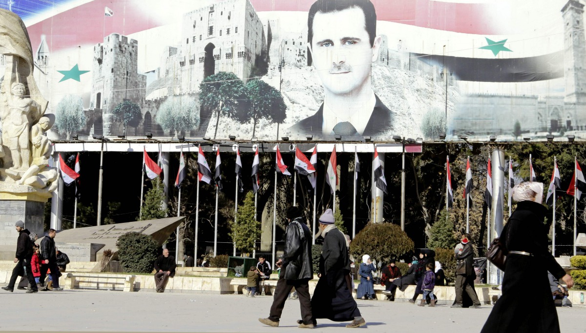 Syrians walk past a poster of Syrian President Bashar al-Assad in Aleppo's Saadallah al-Jabiri Square on January 22, 2017, a month after Syrian government forces retook the northern city from rebel fighters. AFP / Louai Beshara