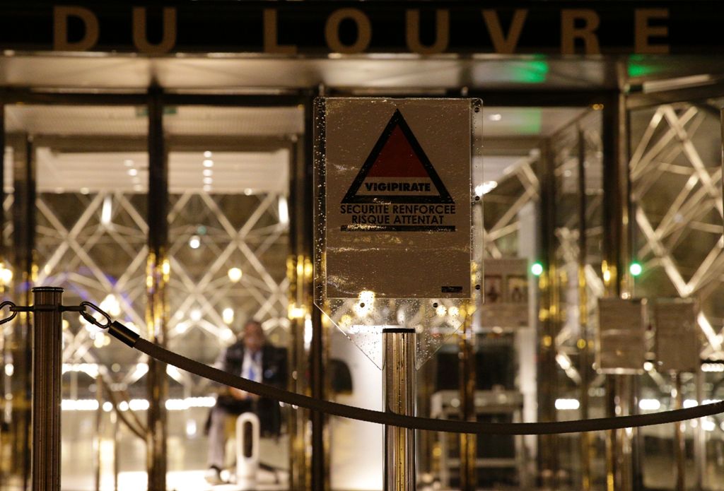 A security guard sits at the entrance of the Louvre Pyramid of the Louvre museum in Paris, on February 3, 2017, as a sign with the symbol of France's national security alert system 