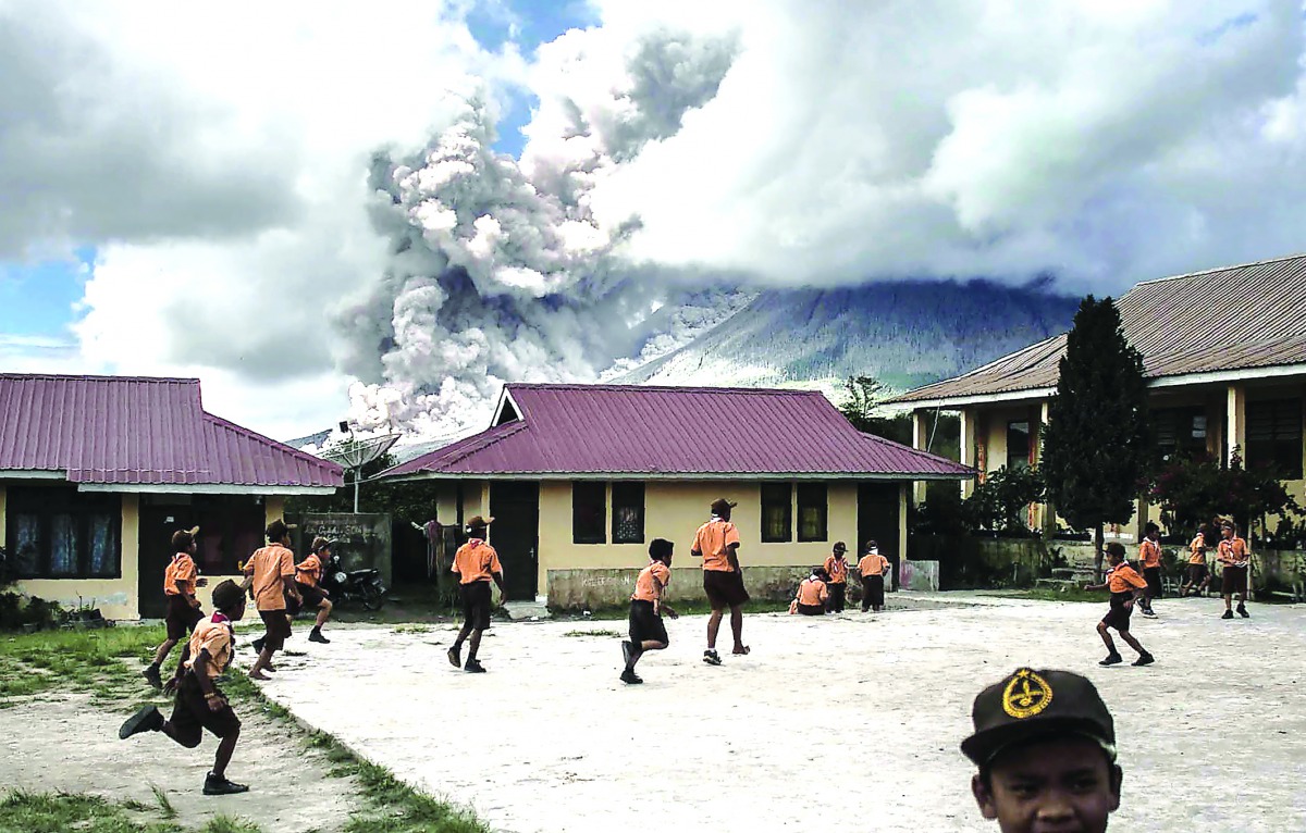 Elementary schoolchildren play outside of their classrooms as mount Sinabung spews thick volcanic ash as seen from Karo, yesterday.