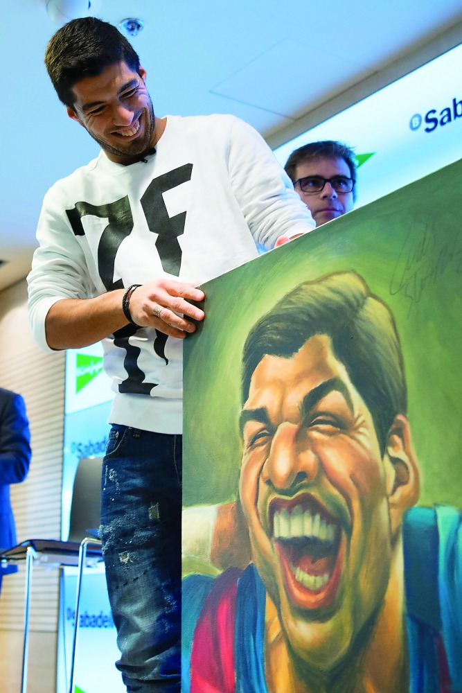 Barcelona striker Luis Suarez smiles as he looks at a caricature of himself by Spanish cartoonist Vizcarra during the presentation of the 12th edition of the book 