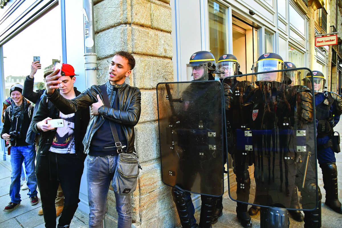 Young men (L) take provocative selfie photos as anti-riot police officers stand guard during a demonstration against police brutality on February 18, 2017 in Rennes, following the alleged rape in the Paris suburb of Aulnay-sous-Bois of a black youth, iden
