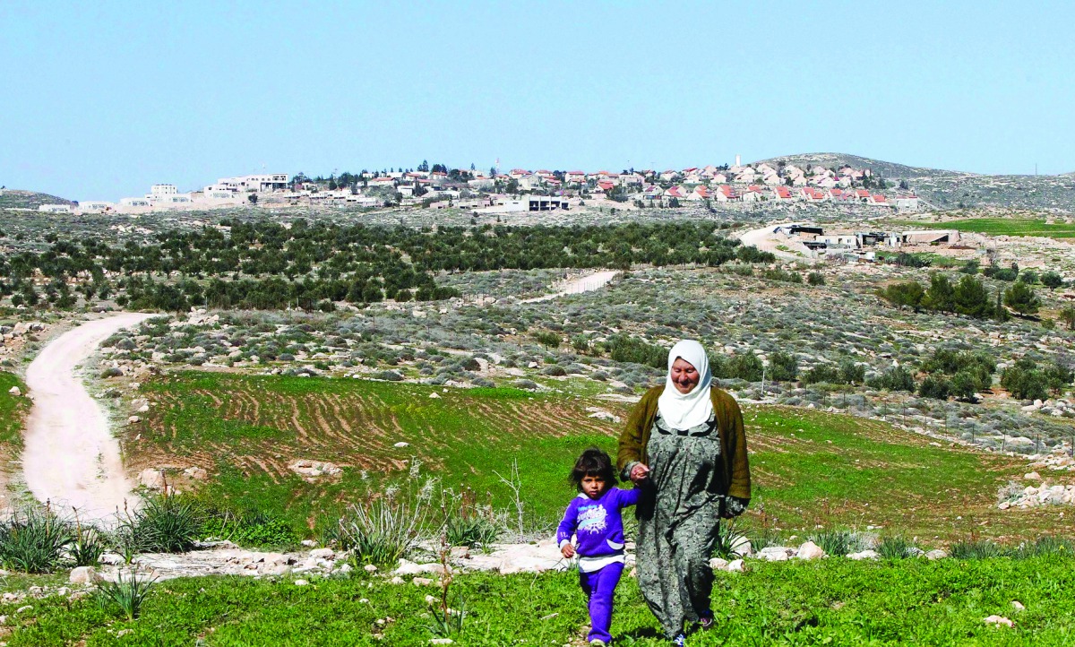 A Palestinian woman and a child walking in the Bani Naaim village with the Israeli settlement of Bani Hever, southwest of the Israeli occupied West Bank city of Hebron, seen in the background.